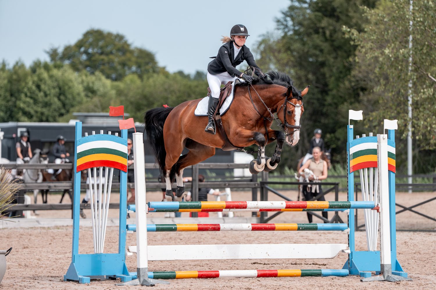 White horse and rider clearing jump at Oslo Horse Show indoor competition.