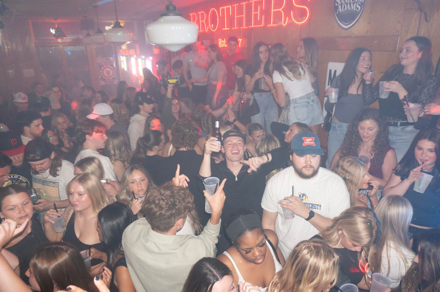 Crowded nightclub scene with neon lights and dancing patrons under 'Brothers' sign.