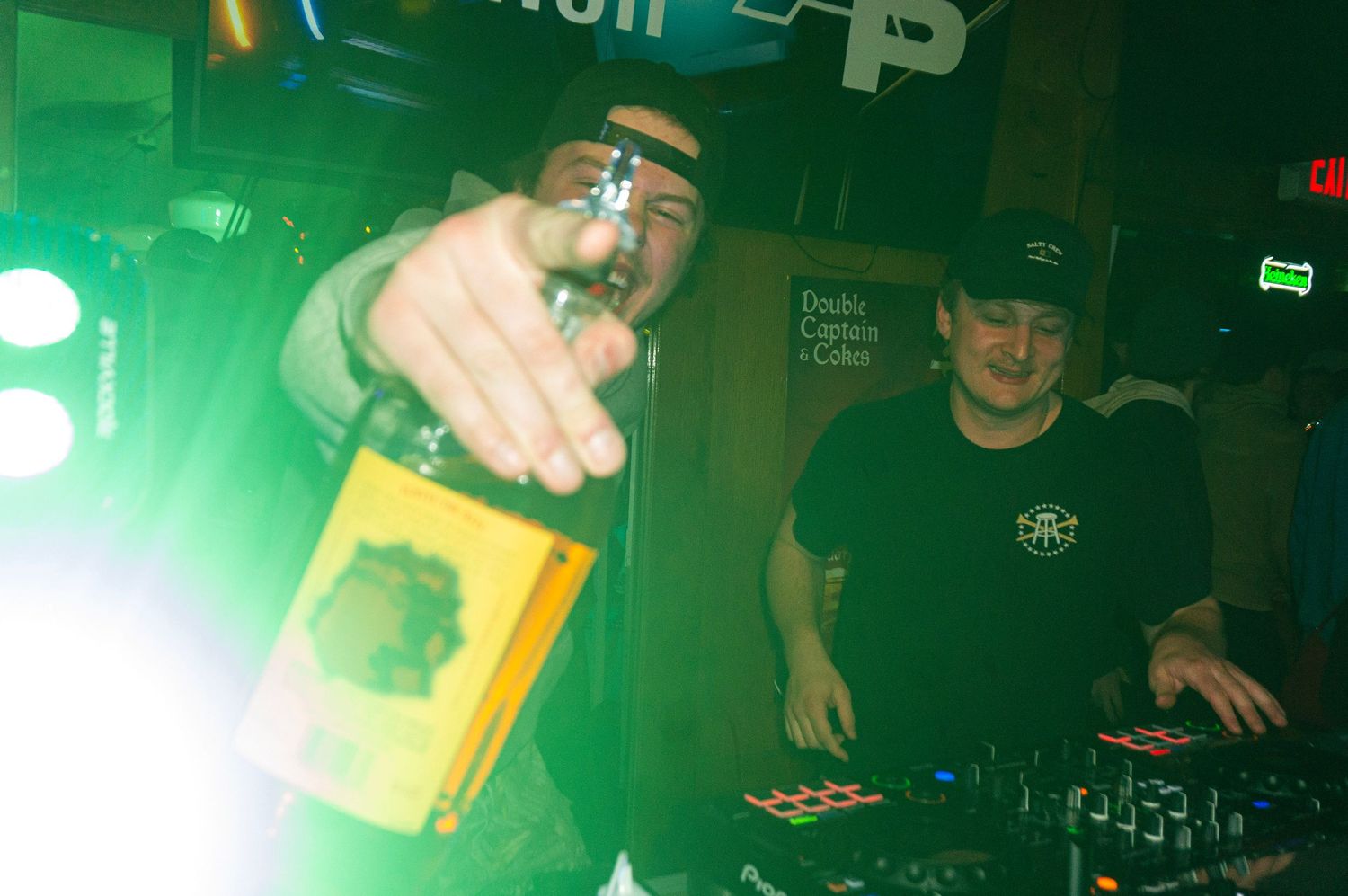 A green-lit nightclub scene shows hands holding drinks and people socializing in a dimly lit atmosphere.
