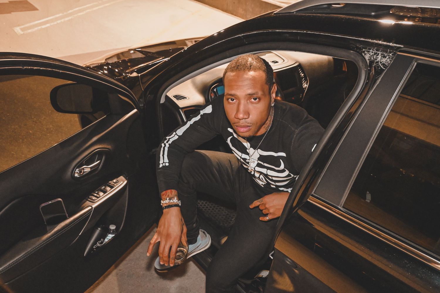 A person in a black jacket sits in the driver's seat of a luxury car at night.