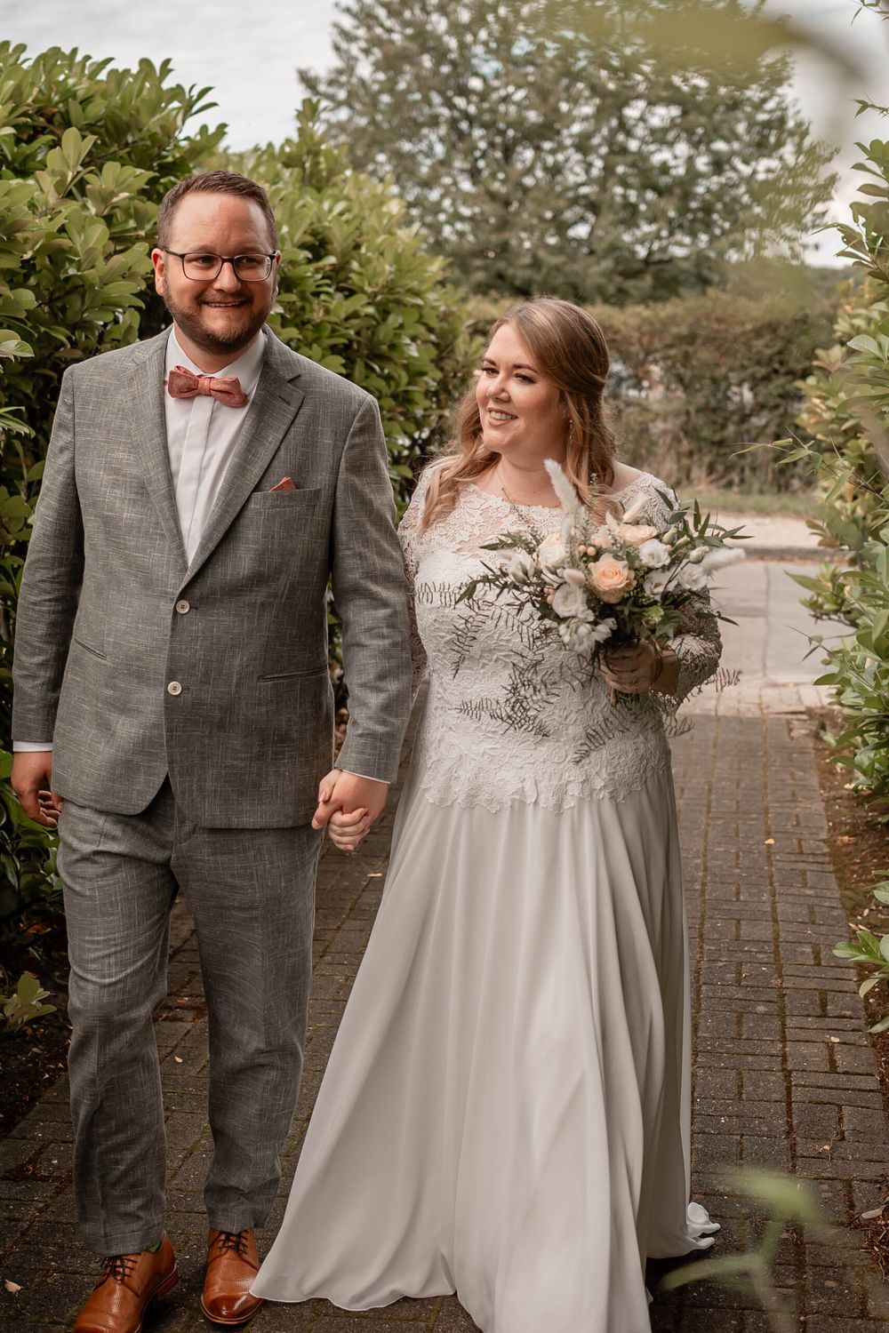 A couple shares candid, joyful moments in outdoor wedding portraits wearing a white dress and grey suit with bow tie.