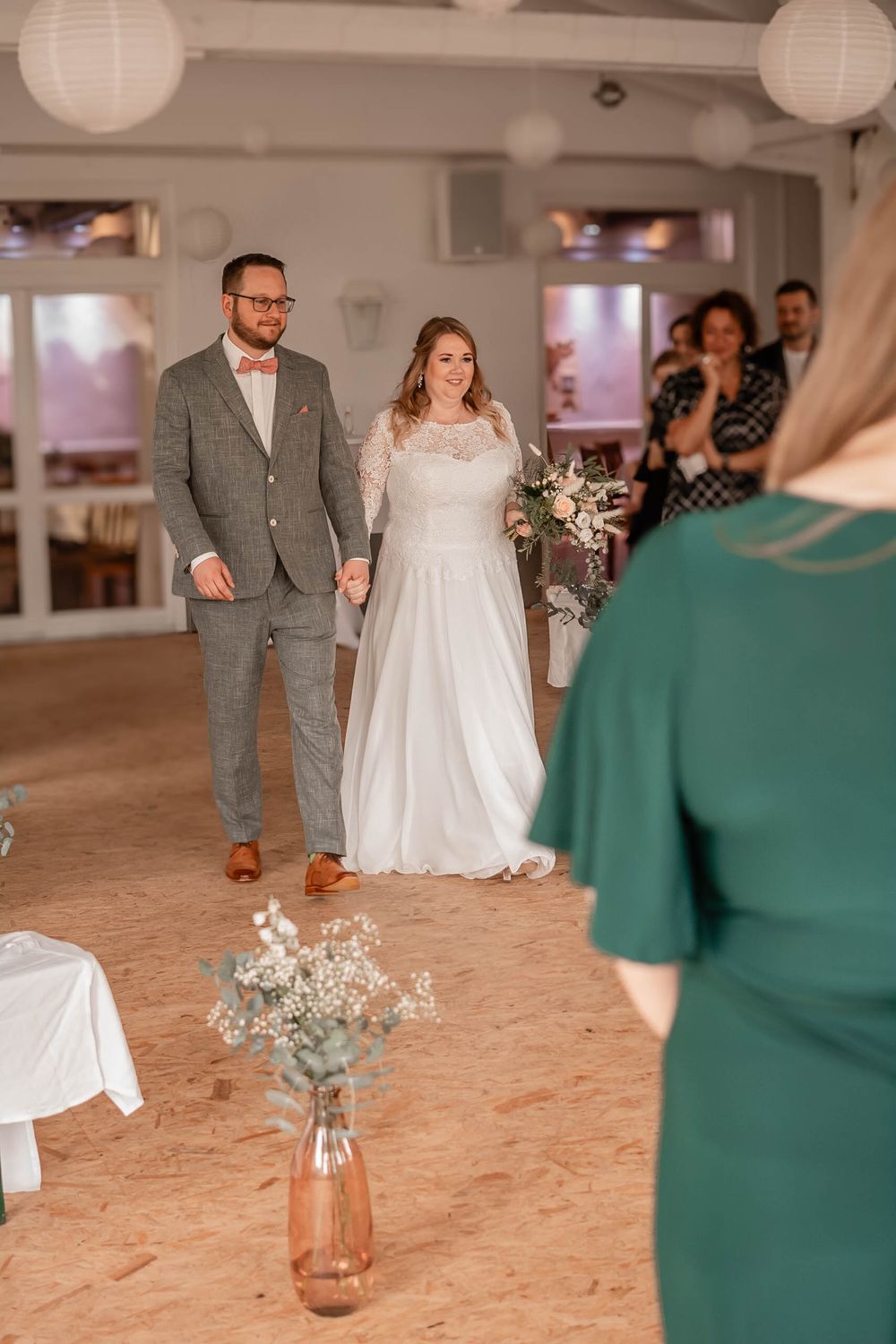 A wedding ceremony taking place in a bright venue with white paper lanterns and floral decorations.