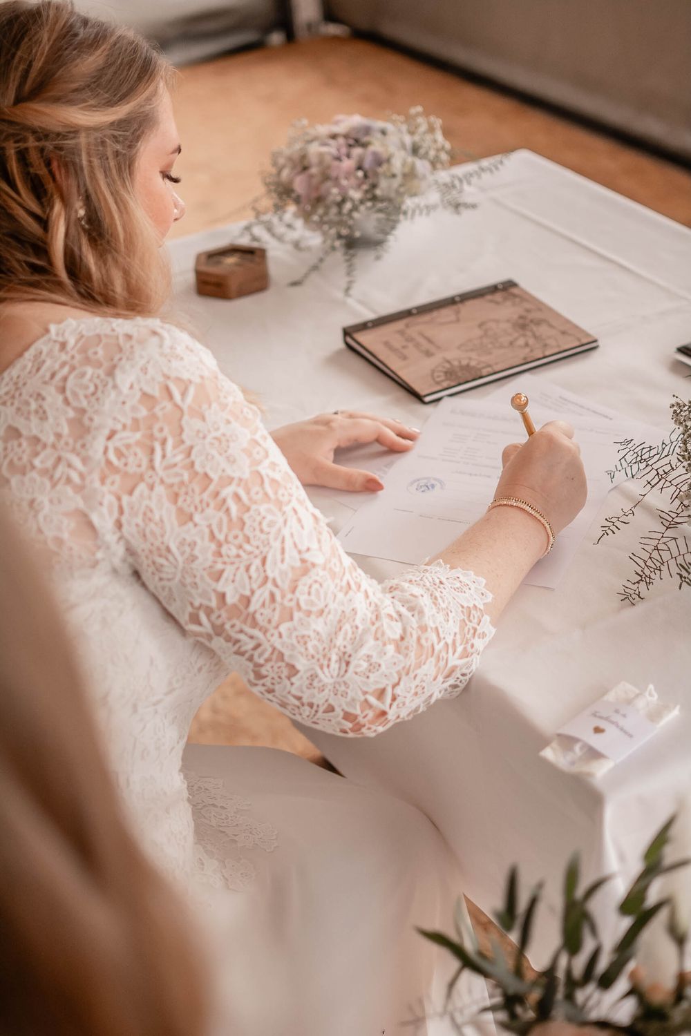 A close-up view of hands in white lace sleeves writing calligraphy at a desk with delicate floral decorations.
