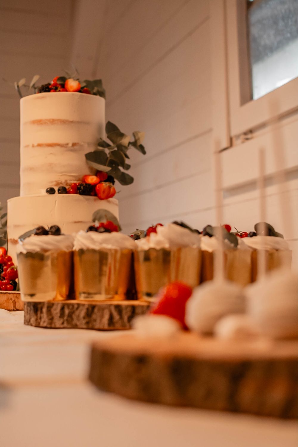 A rustic wedding cake with fresh berries displayed on wooden slices with smaller desserts arranged around it.
