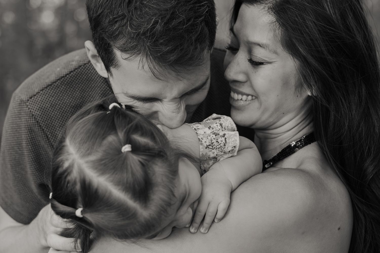 A black and white intimate portrait of a couple embracing their young child in a tender family moment.