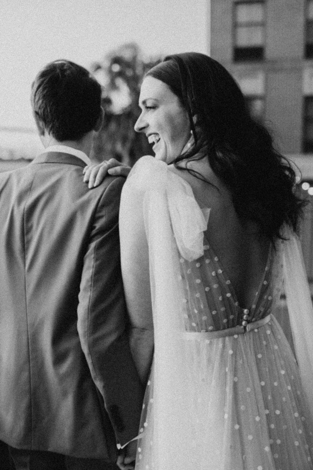 Black and white wedding photo showing a bride's veil with delicate pearl details against a dark suit.