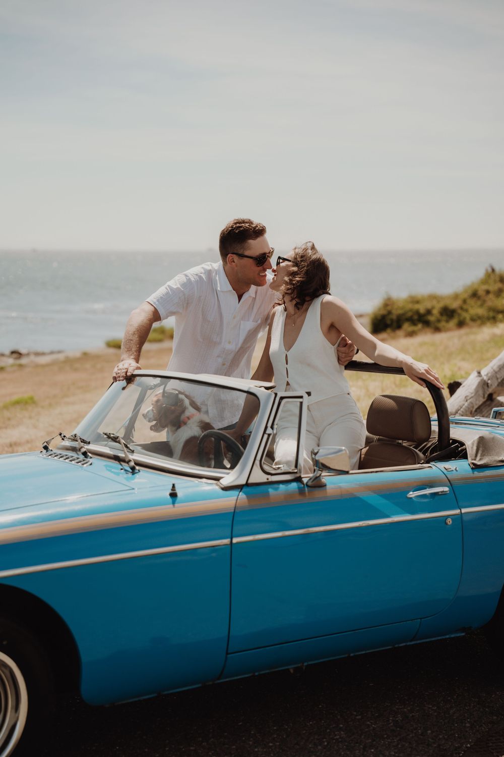 Couple kissing in a vintage blue convertible car by the ocean on a sunny day. Engagement photoshoot. Victoria, BC, Vancouver Island.