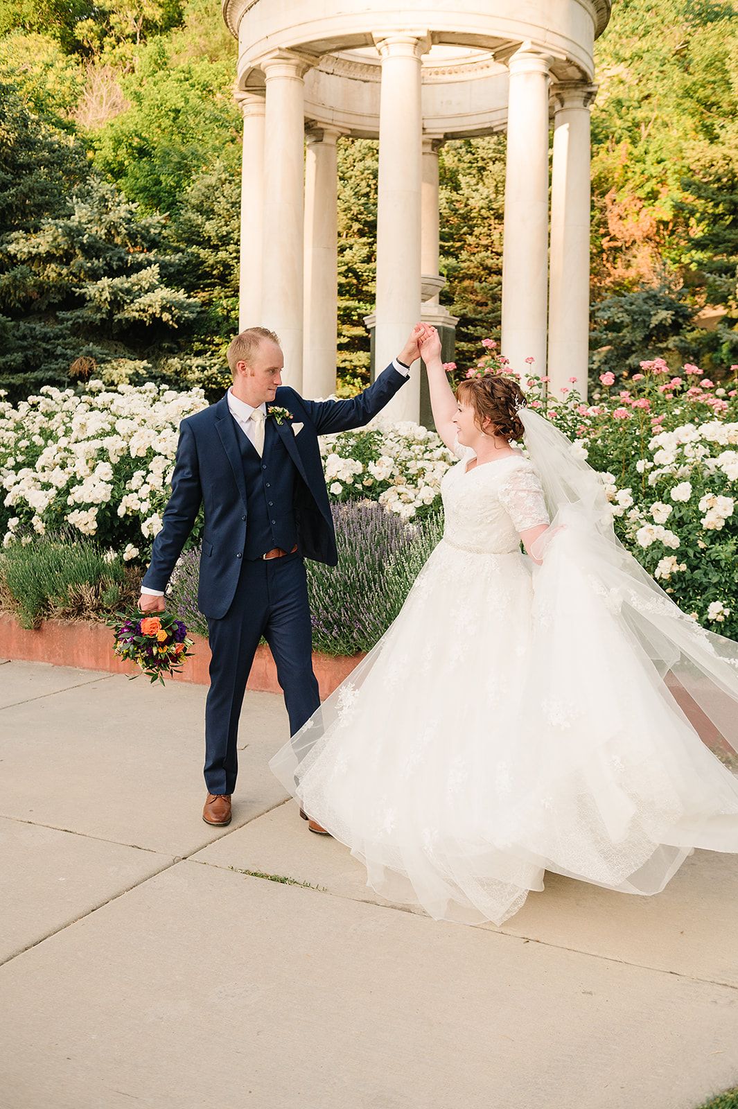 Couple dances under white garden gazebo surrounded by blooming white flowers.