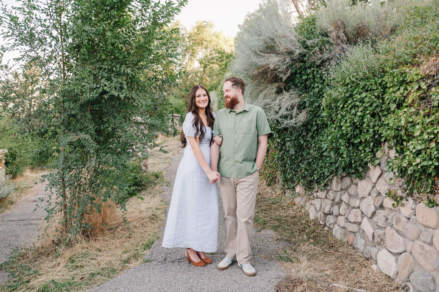 Couple in casual elegant attire standing on stone path in garden setting.
