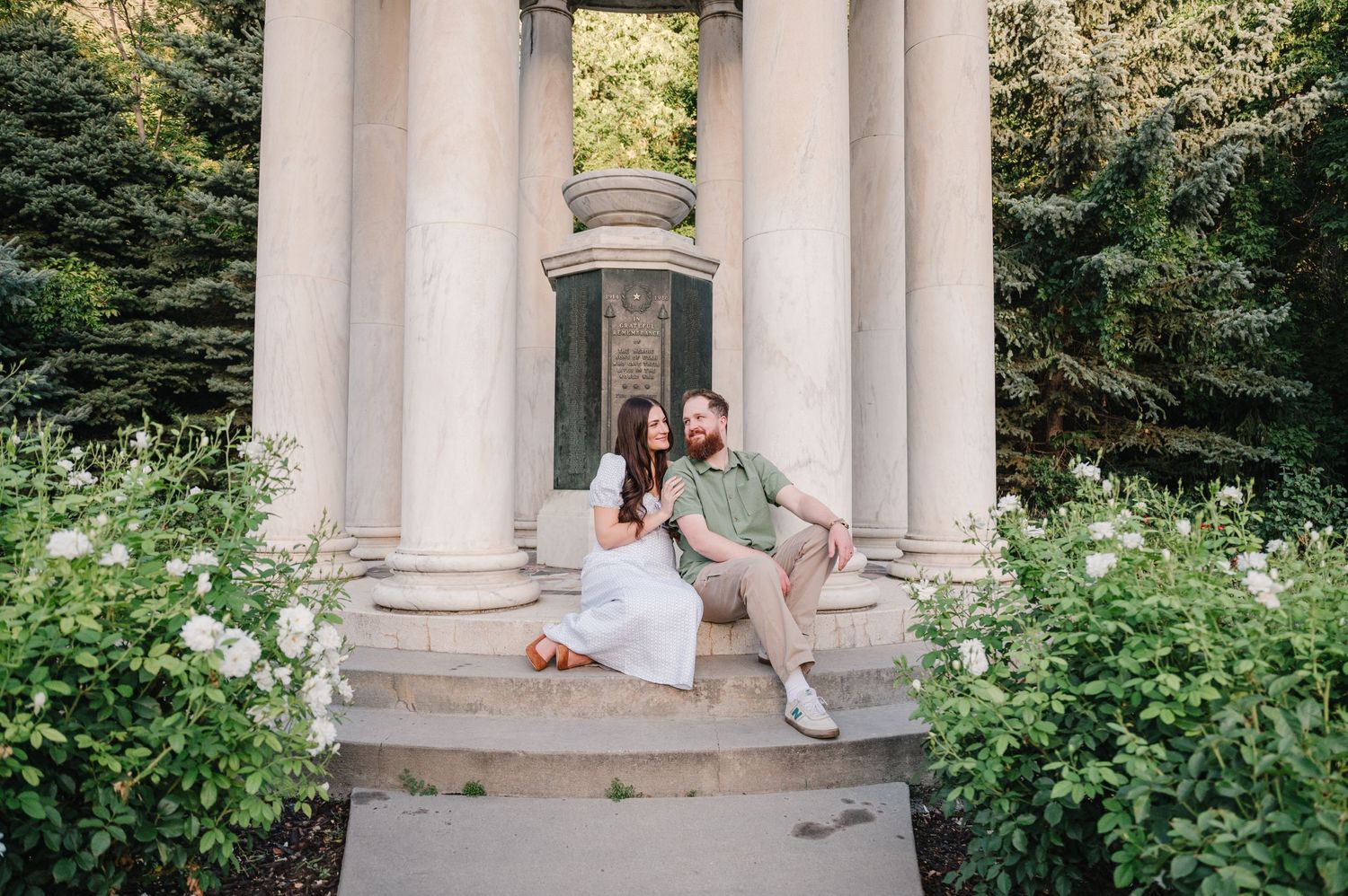 Couple sitting on stone steps of a classical columned structure in garden setting.
