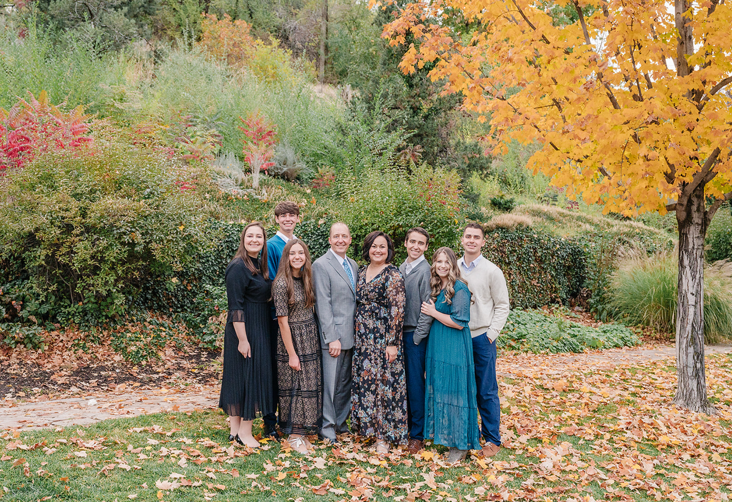 Group gathering amidst vibrant autumn foliage and fallen leaves in an outdoor garden.