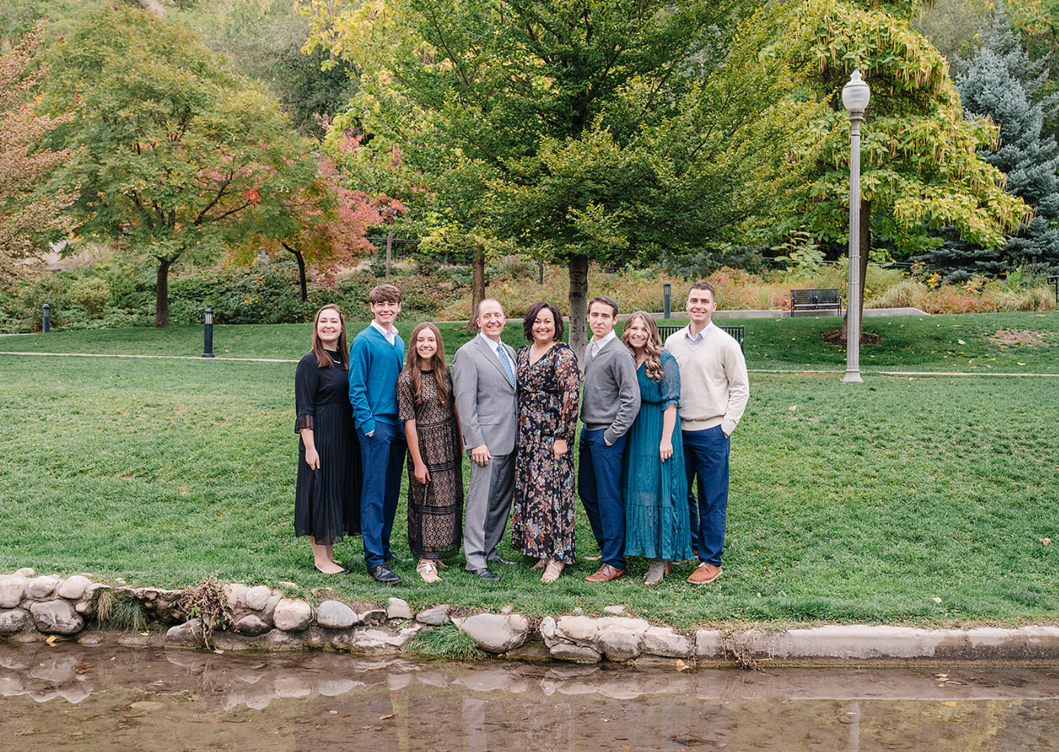 Group photo in a park with stone wall and autumn trees in background.
