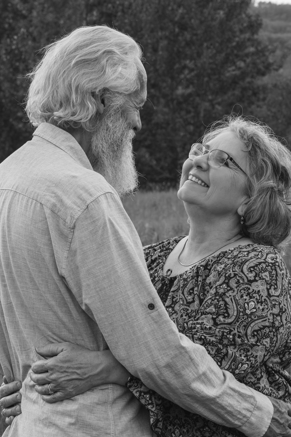 Black and white photo of a happy elderly couple embracing and smiling at each other outdoors.