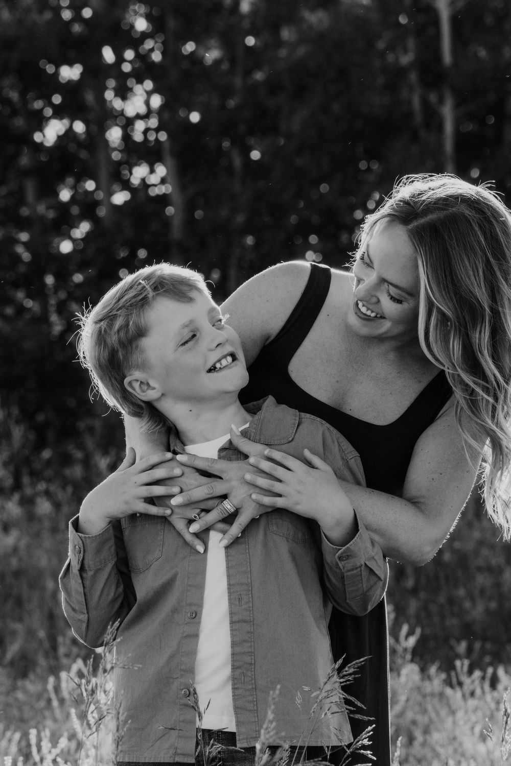 Black and white photo of a laughing mother hugging her young son outdoors in a field.