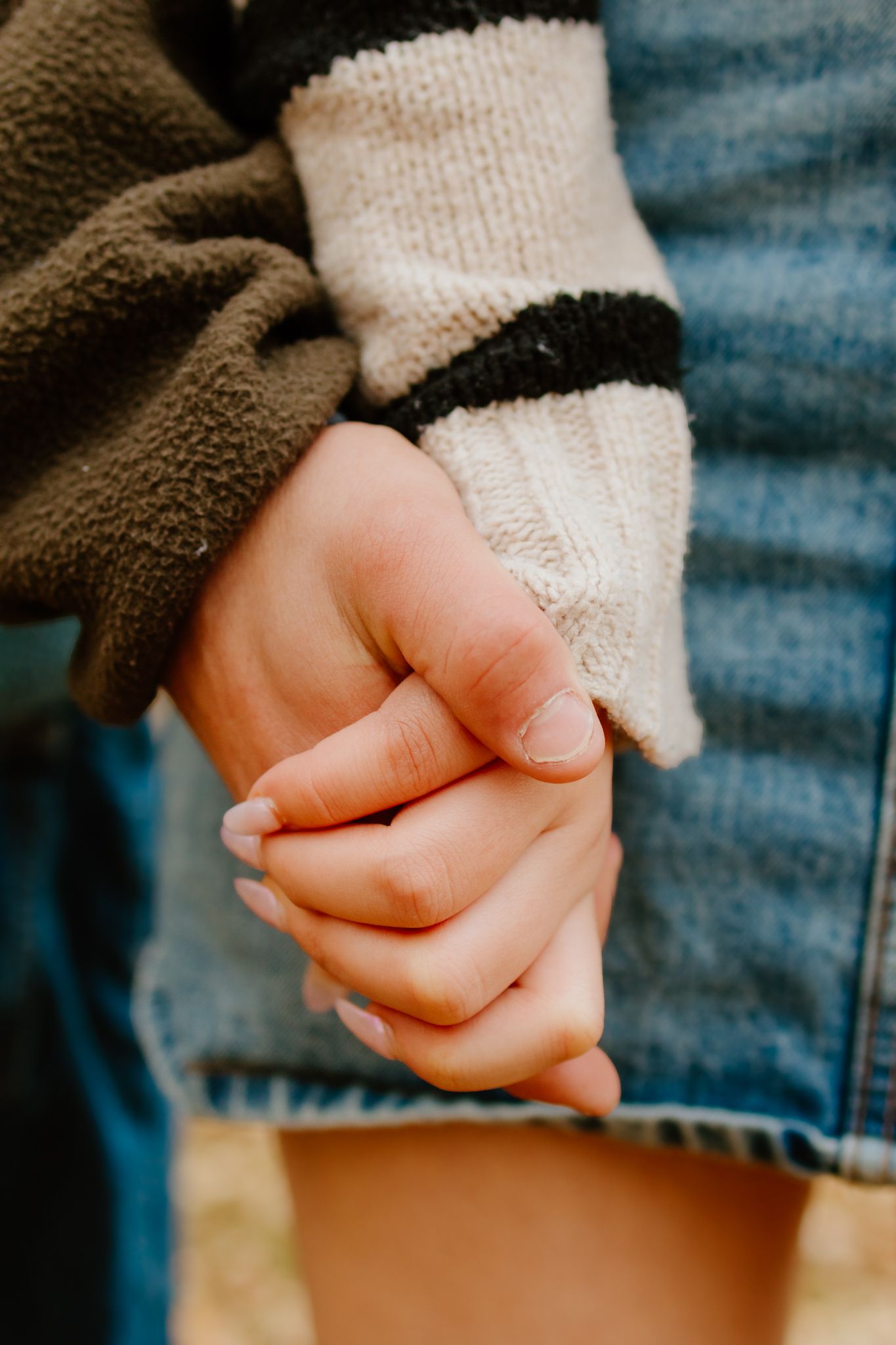 Two teenagers holding hands in autumn, wearing cozy sweaters and denim.