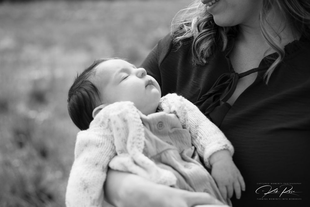 Black and white photo of mother cradling sleeping newborn baby wrapped in soft blanket outdoors.