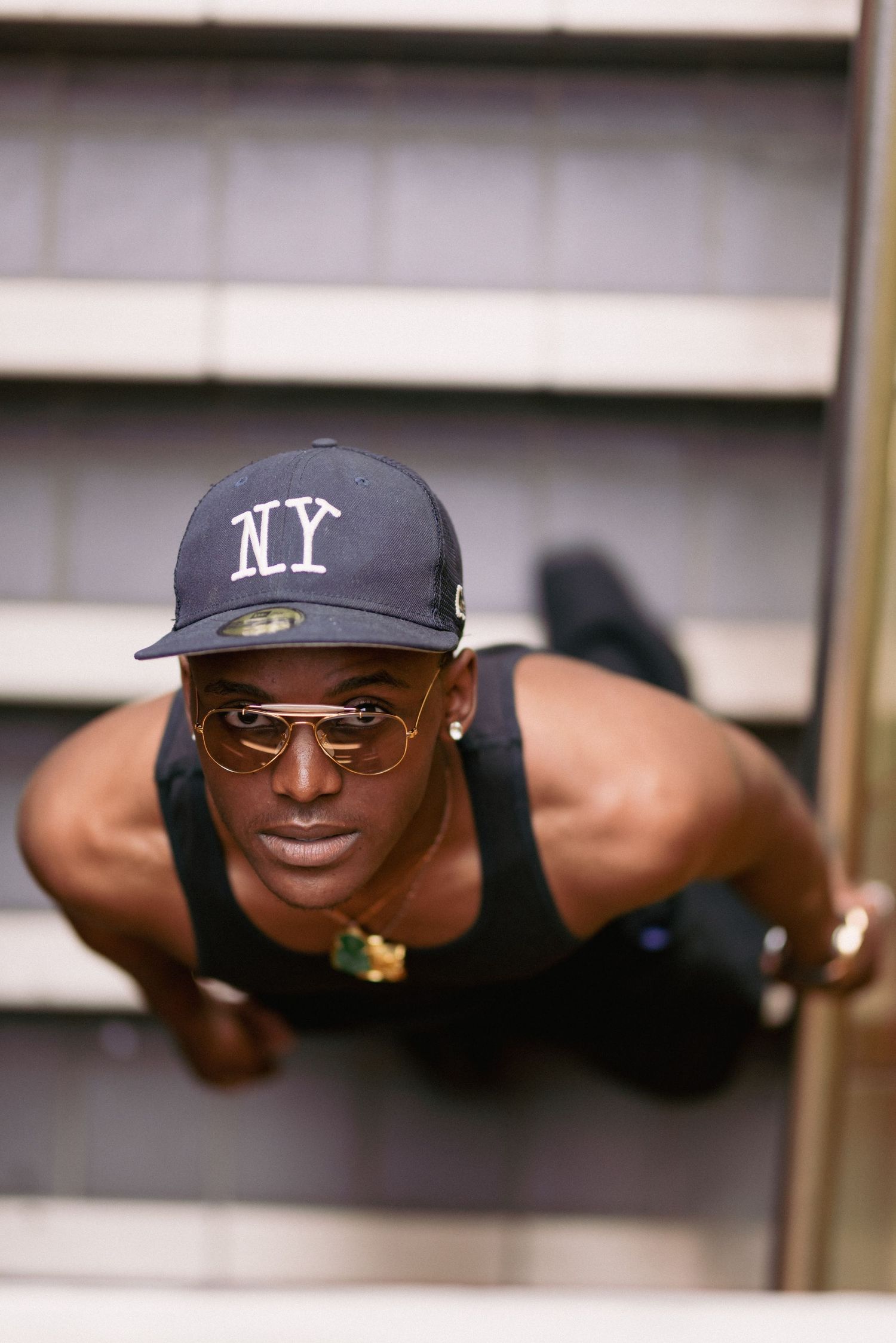 Person in NY cap and tank top doing push-ups while wearing sunglasses.