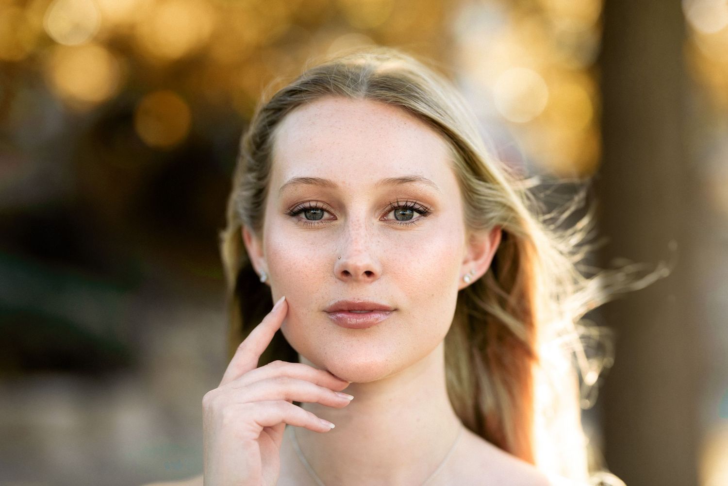 Soft beauty portrait with wind-swept hair against golden background.