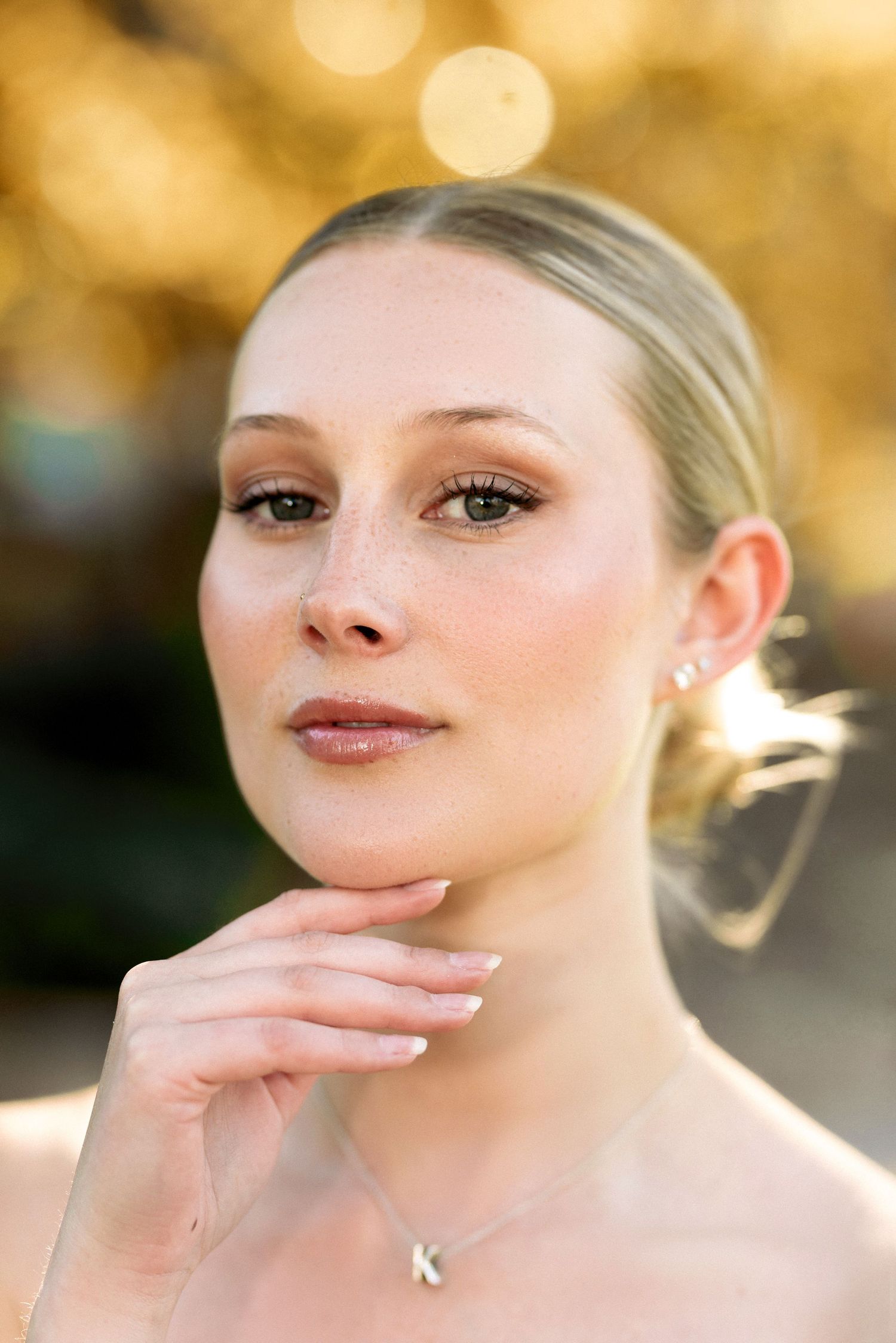 Elegant portrait with hand posed near chin against warm bokeh background.
