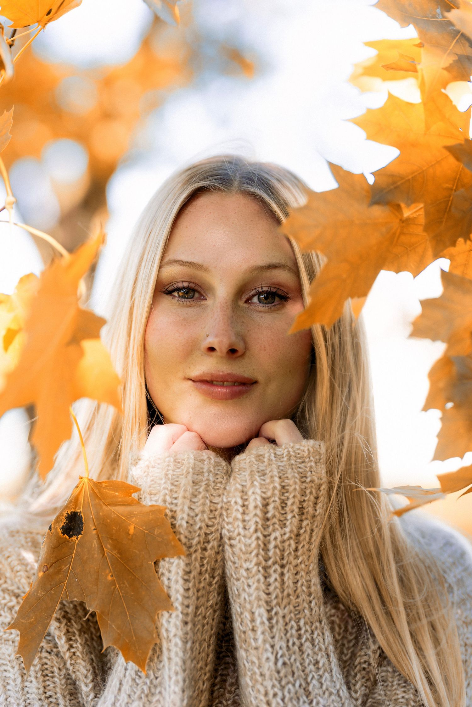 Fall portrait with cozy sweater and maple leaves against bright background.