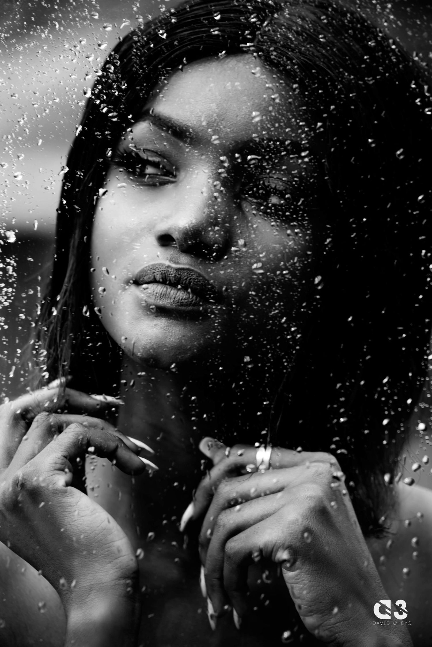 Artistic black and white portrait through rain-covered glass with dramatic lighting.