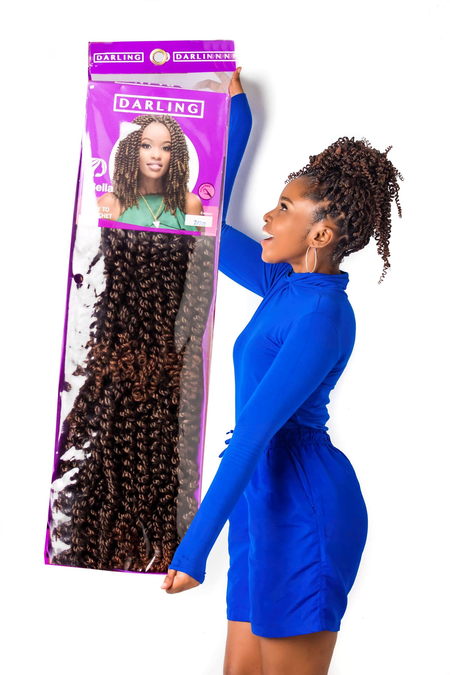 Model in blue dress holding up packaged hair extensions while posing against blue background.