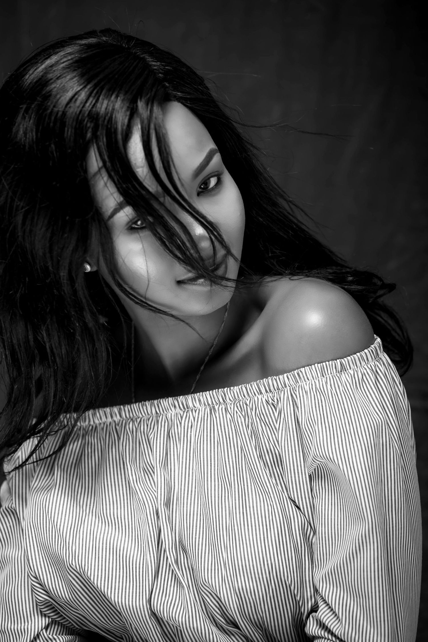 Dramatic black and white portrait in off-shoulder striped top with windswept hair.