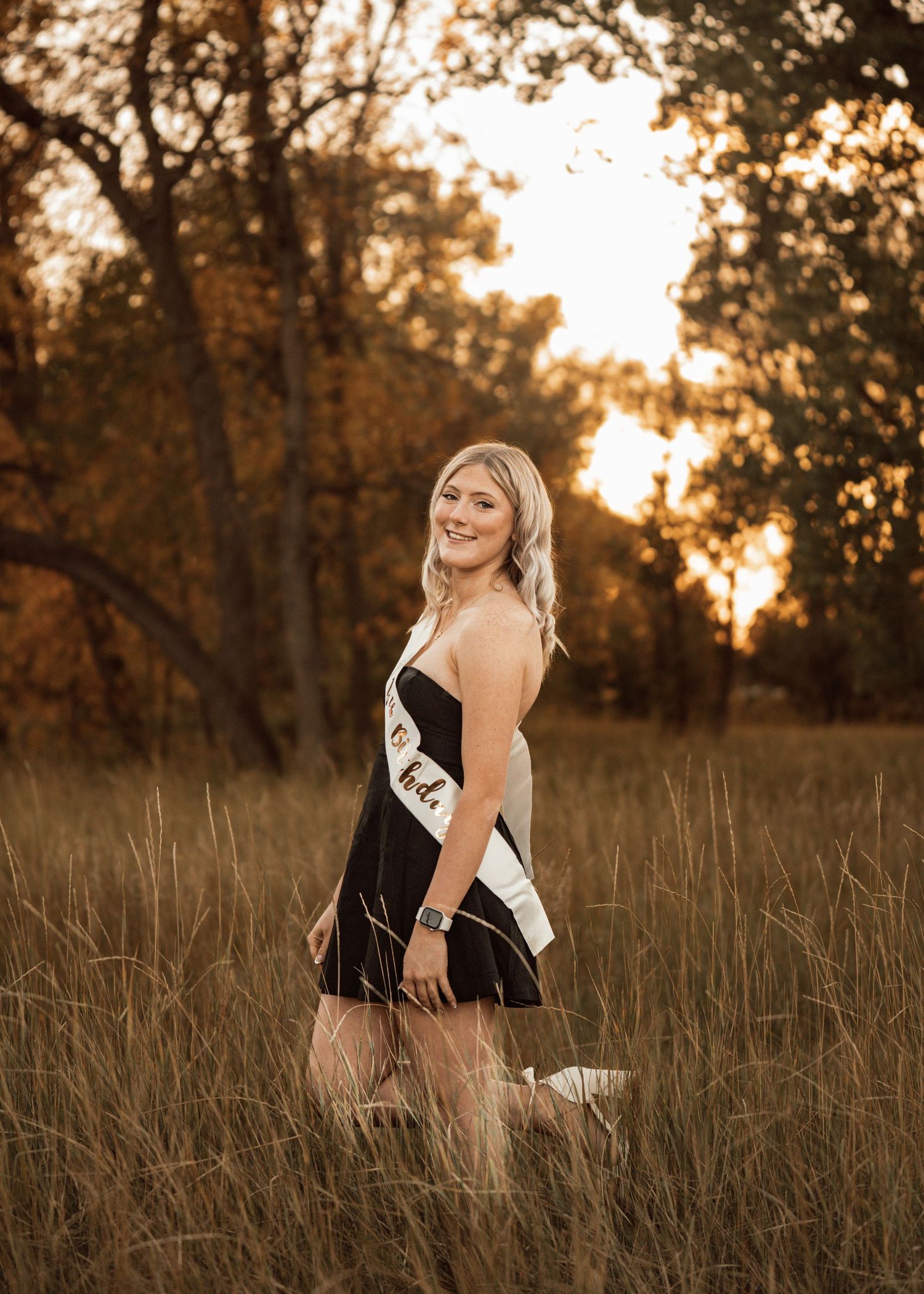 Person poses joyfully in grassy field during sunset photoshoot.