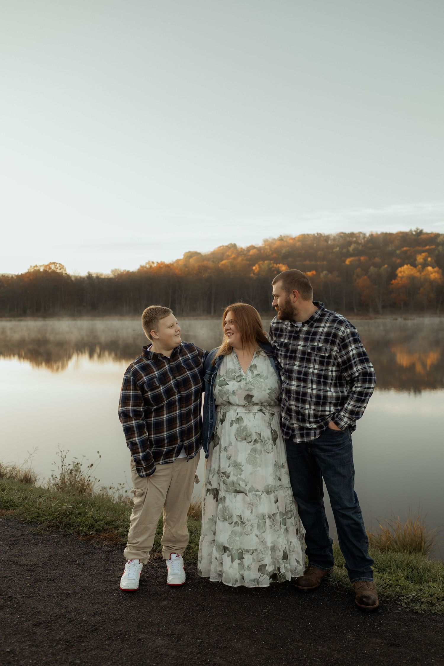 Family shares tender moment amongst fallen autumn leaves in forest setting.