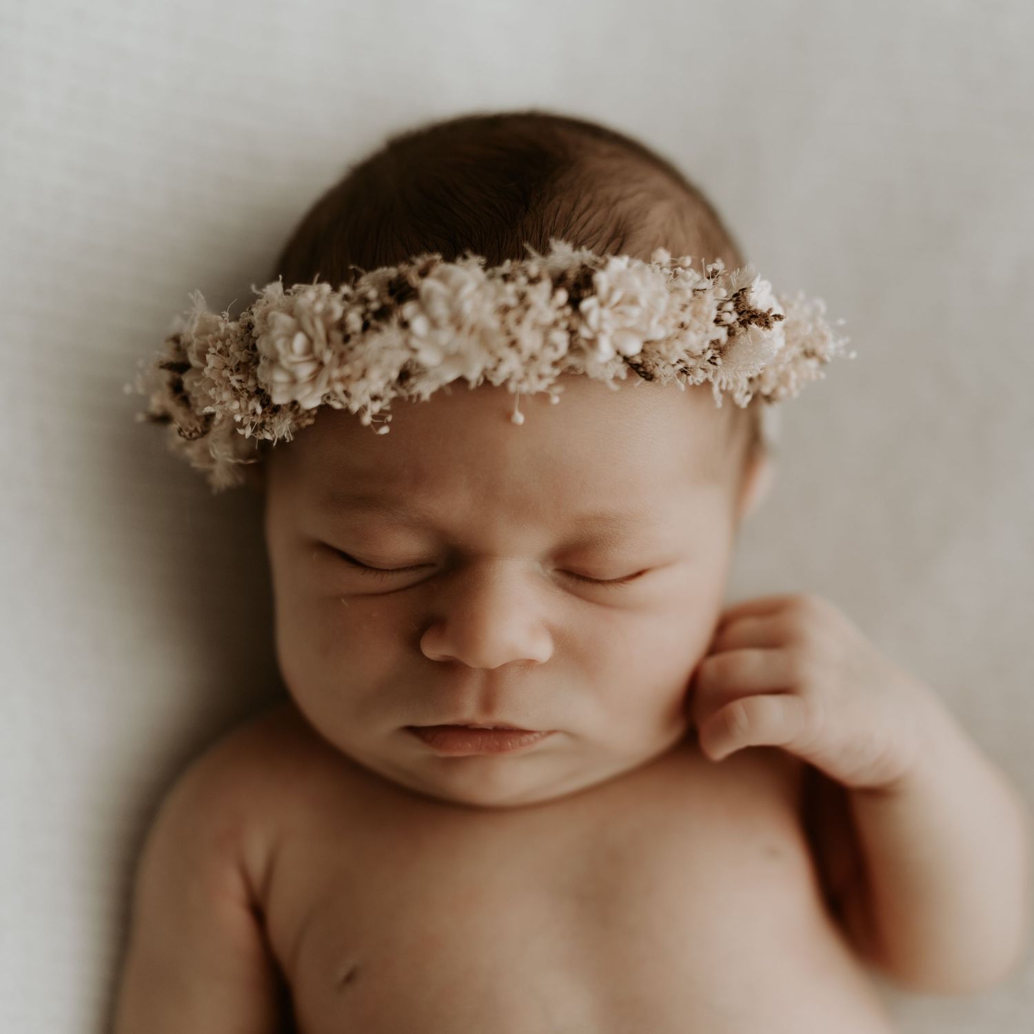 Close-up portrait of a sleeping newborn baby wearing a delicate floral crown.