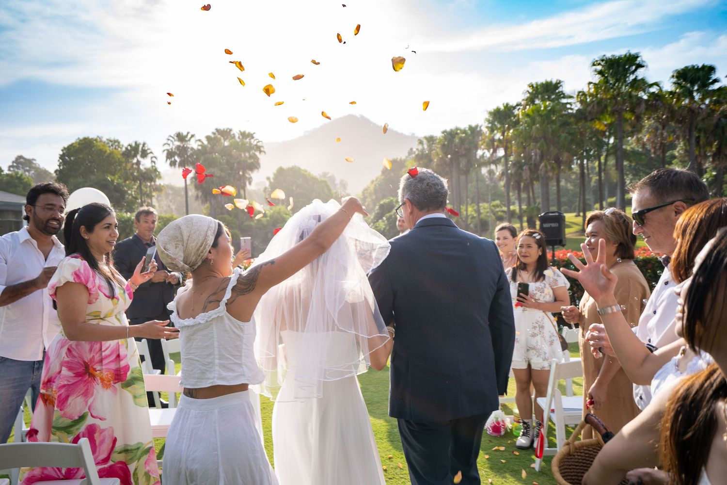 Wedding guests tossing rose petals during an outdoor celebration.