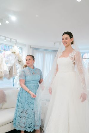 Woman in light blue lace dress viewing wedding gowns in a bridal boutique.