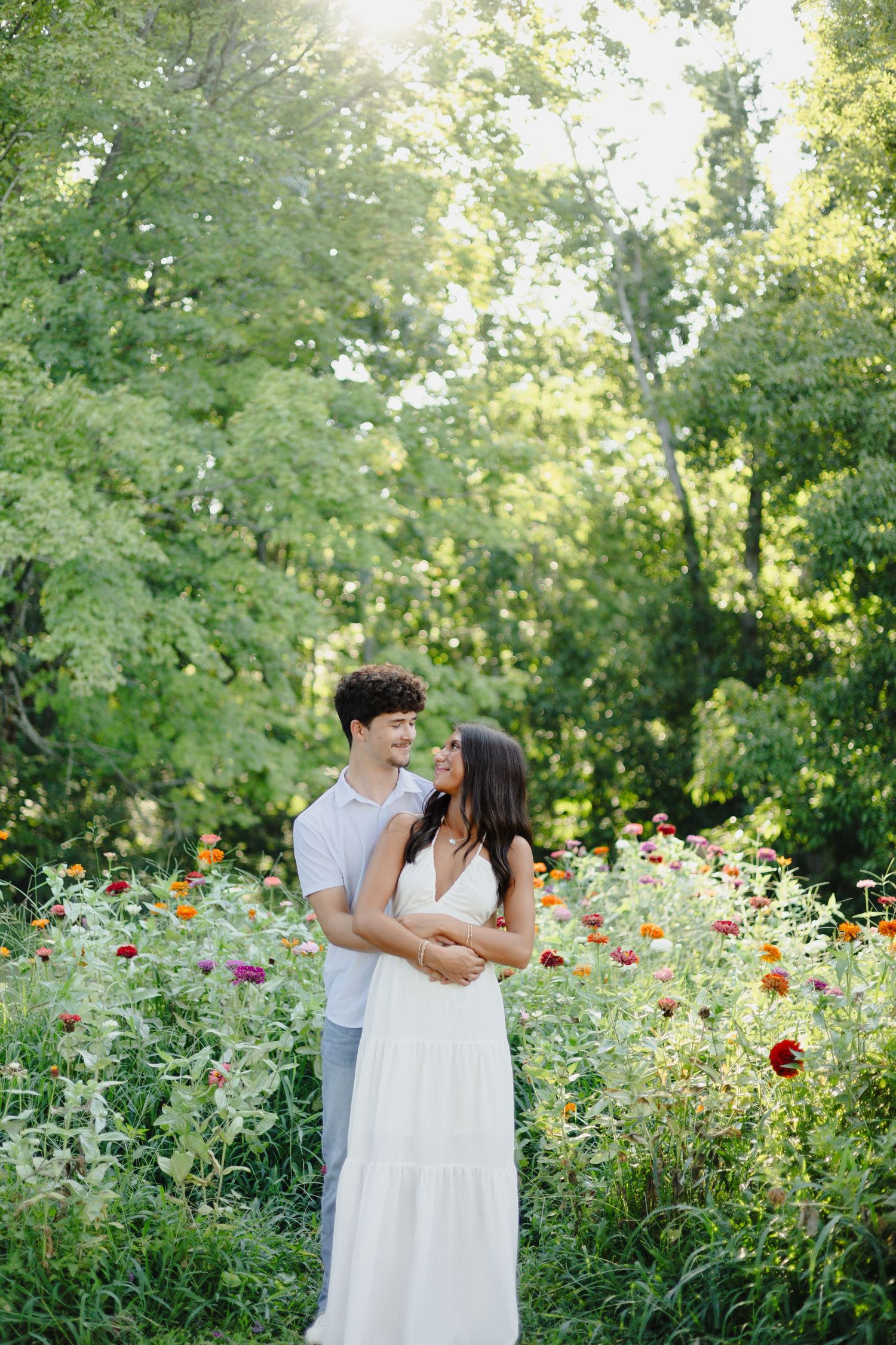 A woman in a white dress holds a child in a grassy field on a sunny day.