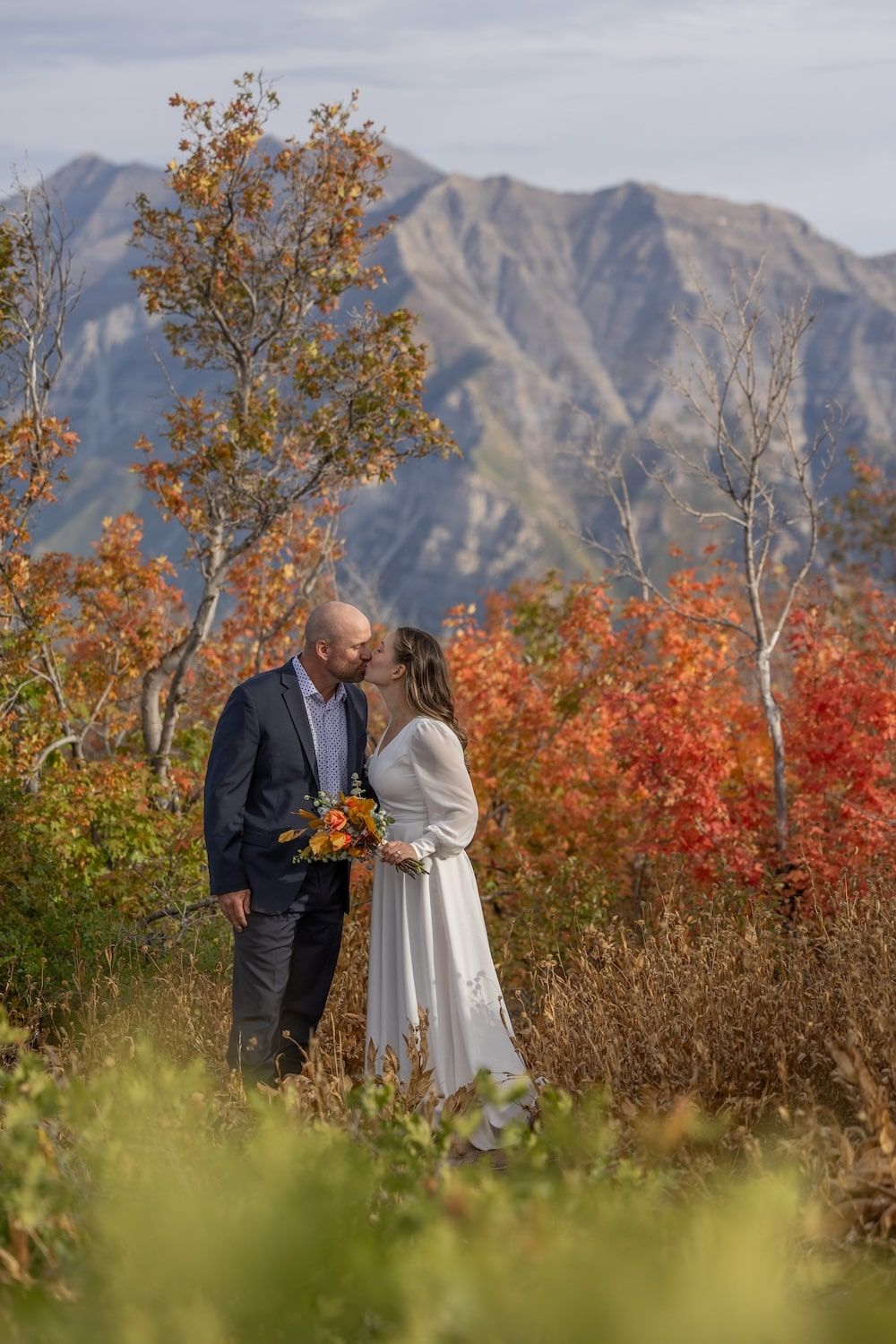 A couple shares an intimate moment surrounded by vibrant fall foliage and majestic mountain backdrop in autumn.