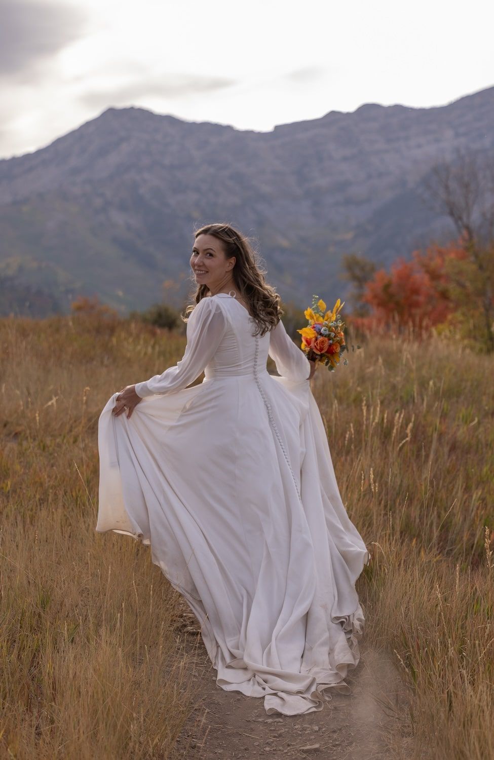 A person in a flowing white dress twirls in a mountain meadow surrounded by fall colors and mountain views.