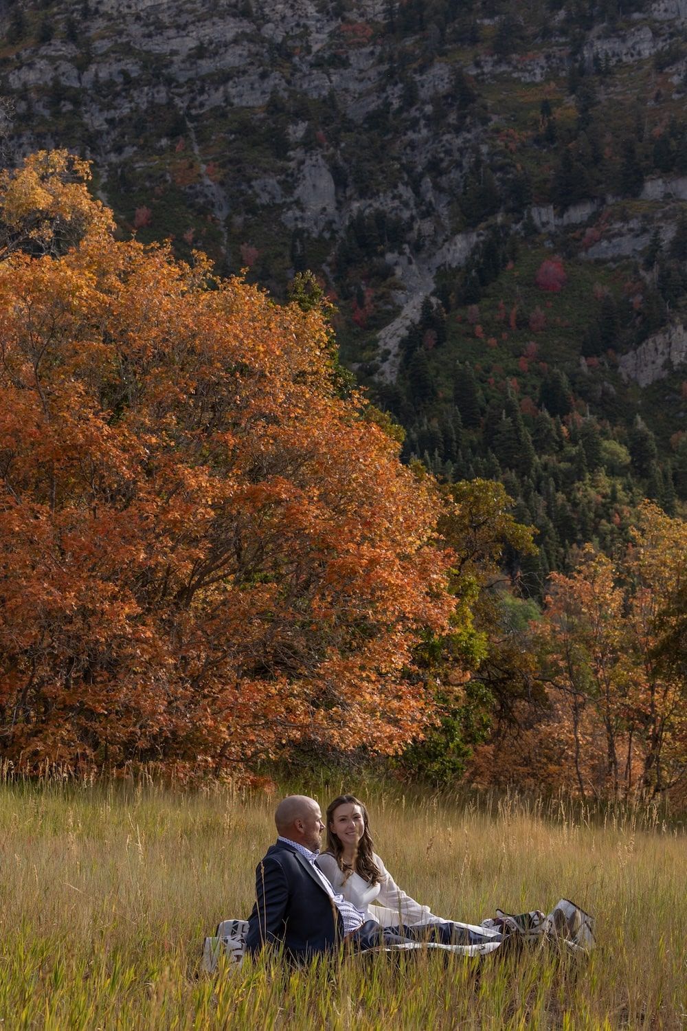 Couple enjoying an autumn day in a mountain meadow with colorful fall foliage and rugged peaks in the background.