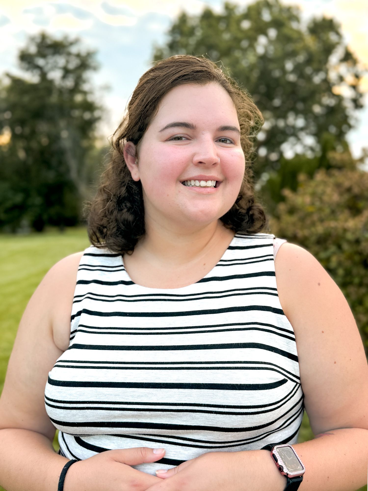 Woman in a striped sleeveless top smiles outdoors on a sunny day.