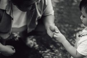 Black and white photo of adult and toddler sharing a tender moment outdoors, exchanging a small object.