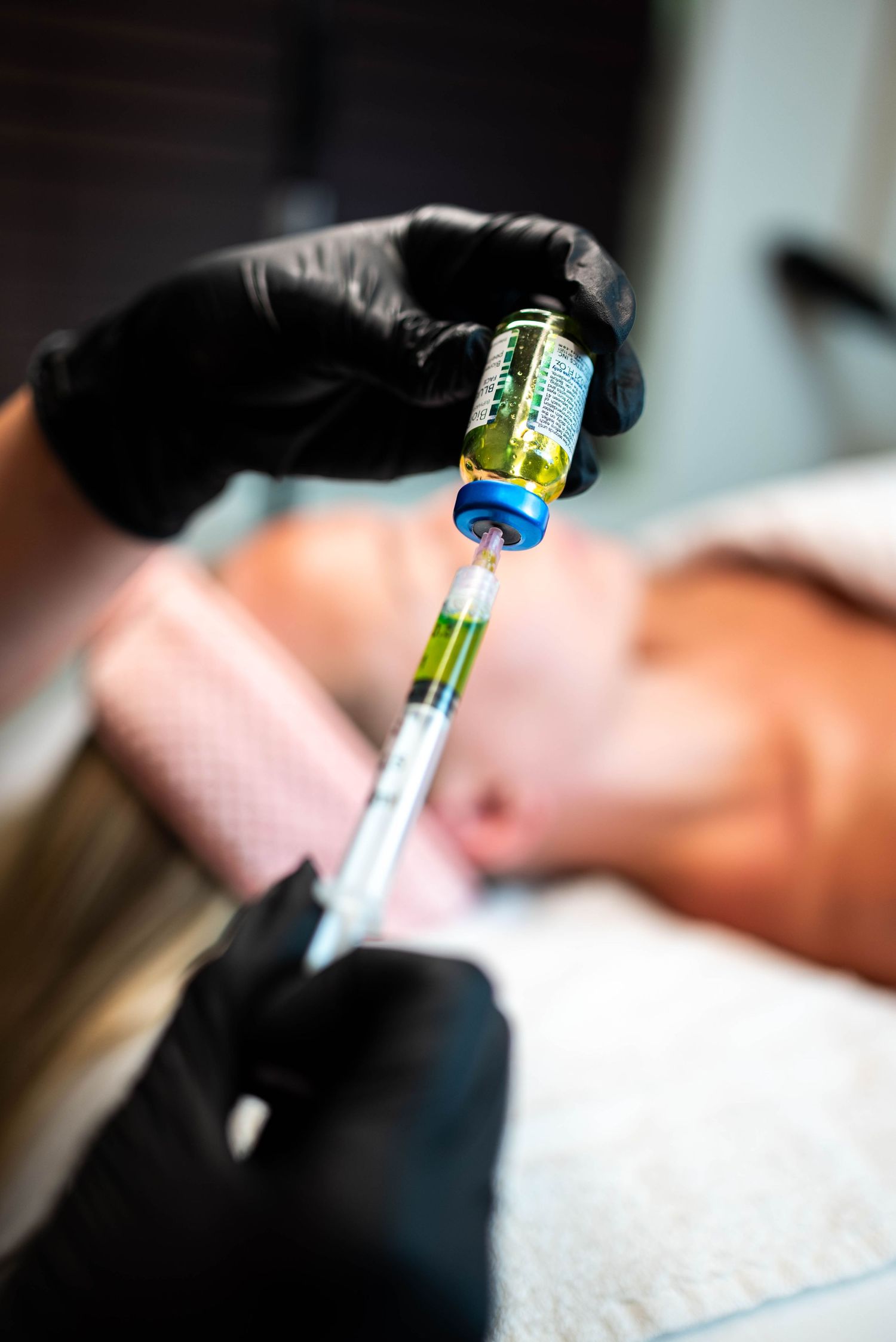 Hands in black gloves preparing a medical injection with yellow liquid.