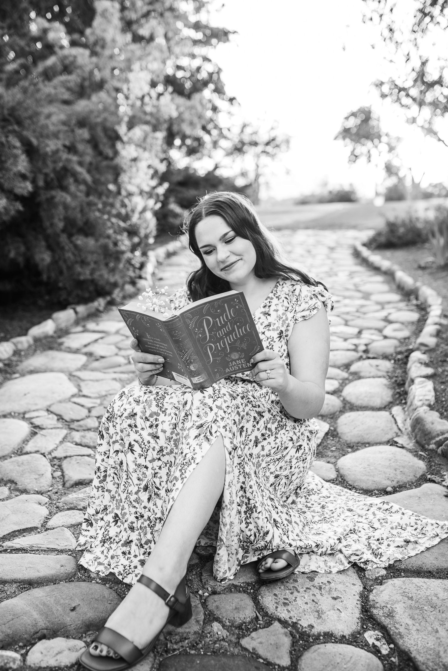 Person reading a book while sitting on a stone path in black and white photograph.