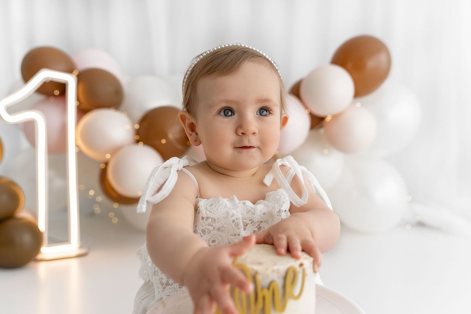 First birthday celebration with balloon arch display in neutral tones.