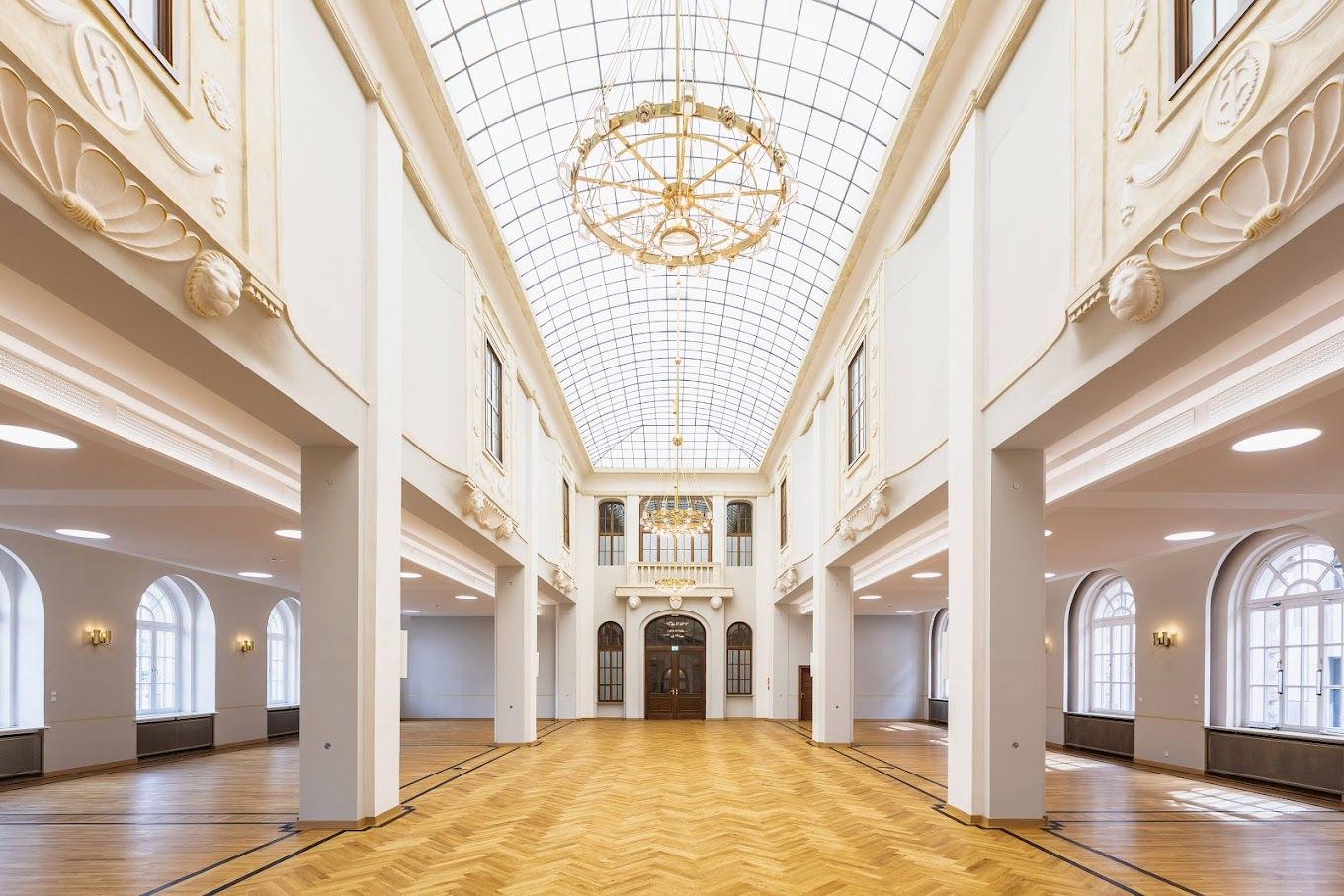 Grand hall with skylight ceiling, white columns and polished floors showcasing classical architecture.