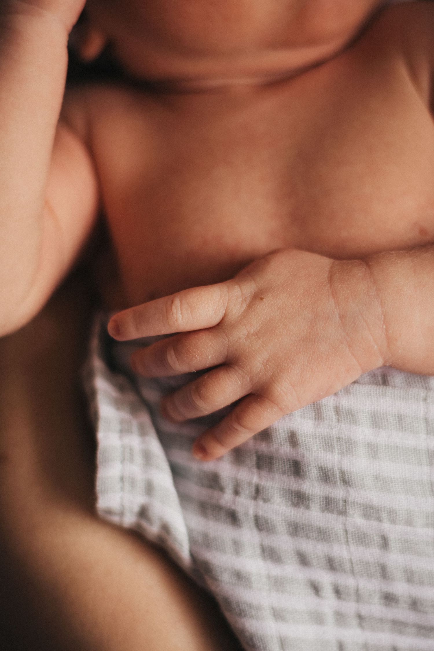 Close up of a newborn's tiny hand against striped fabric.