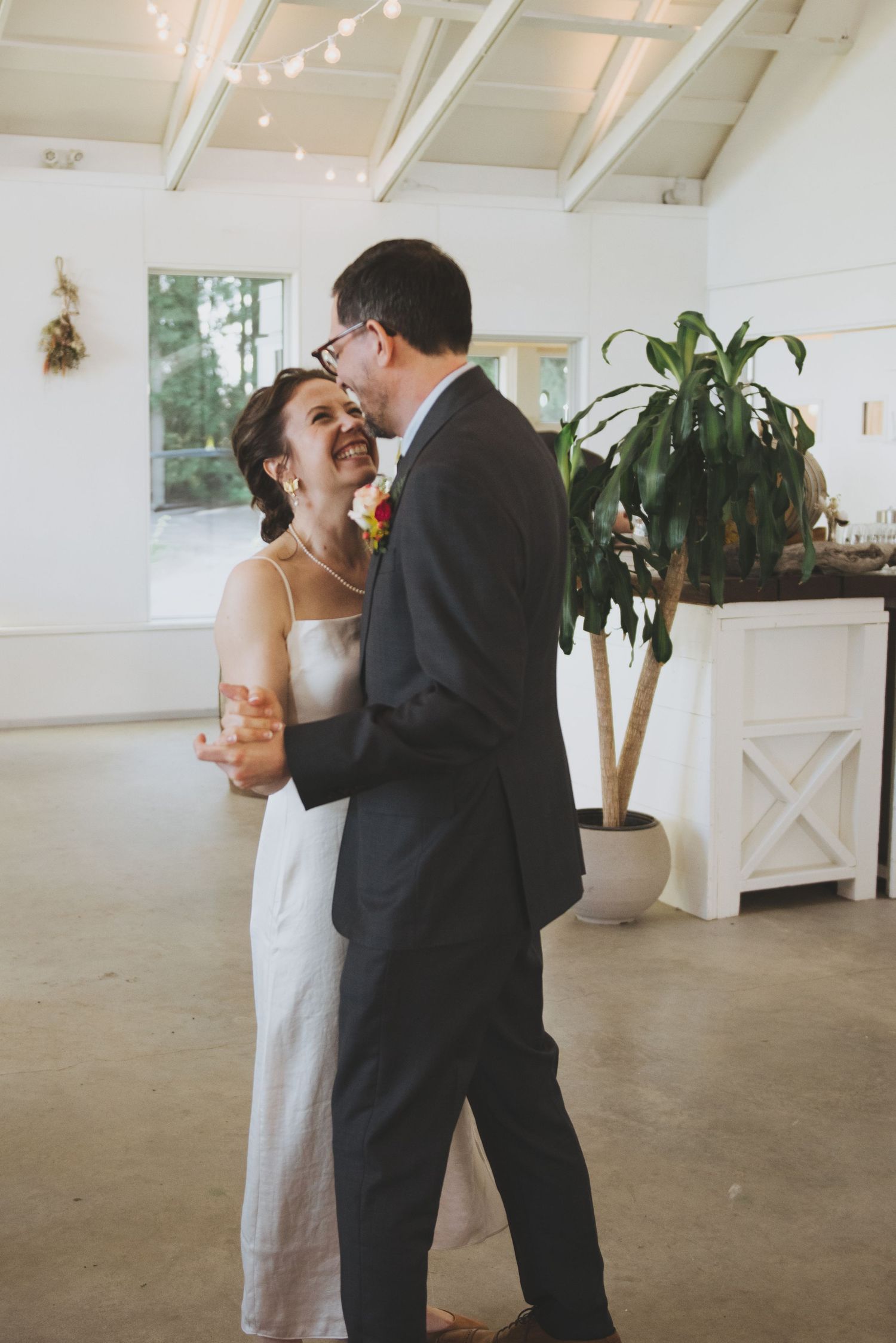 Couple sharing an intimate moment while dancing in a bright reception hall with indoor plants.