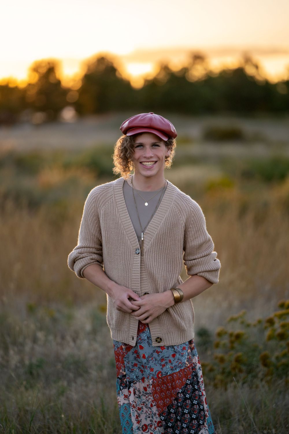 Portrait of someone wearing a burgundy hat and cardigan in a golden sunset field. High school senior.