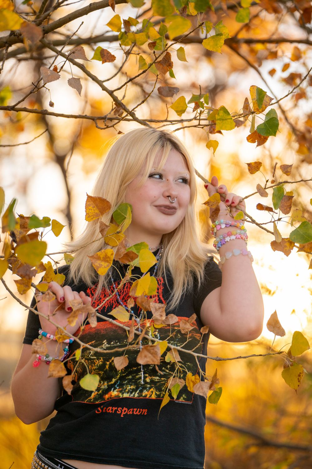 Young woman in black t-shirt poses with autumn leaves in golden sunlight. High school senior.