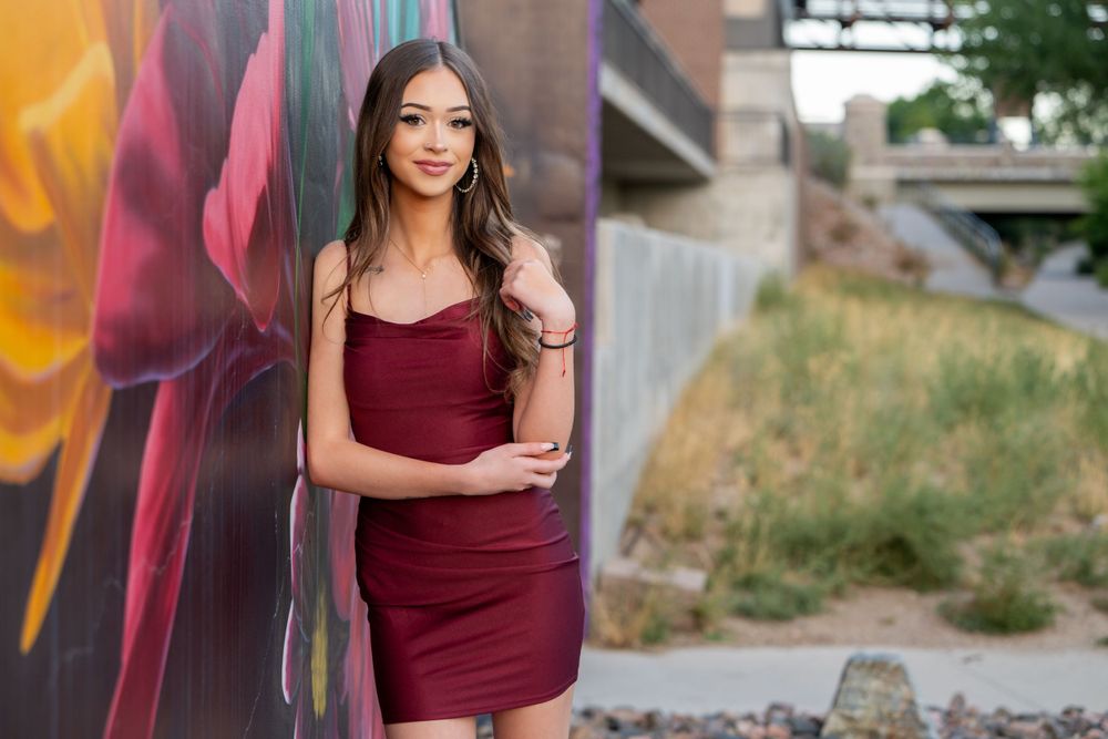 A portrait against a colorful graffiti wall featuring someone in a burgundy dress. High school senior.