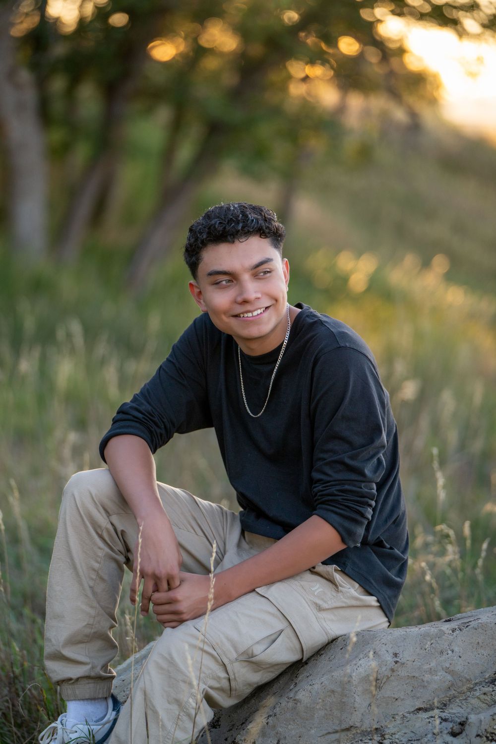 A casual portrait of someone sitting on rocks at sunset wearing a black sweater and khaki cargo pants. High school senior.
