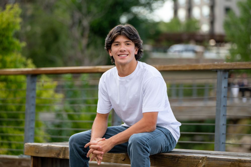 An outdoor portrait on a wooden bench with greenery in the background. High school senior.