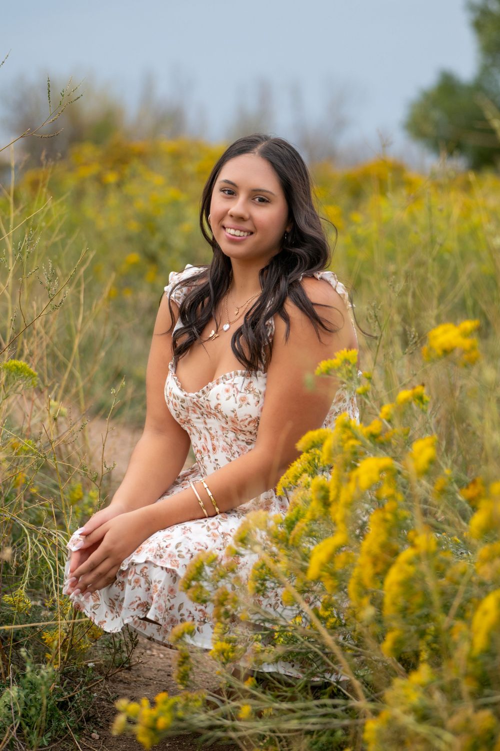 A summer portrait in a field of yellow wildflowers with someone wearing a floral dress. High school senior.